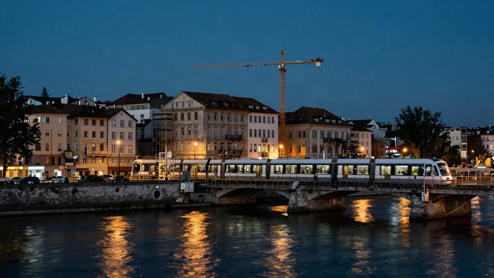 A tram crossing a stone bridge in a historic European river city, a crane behind